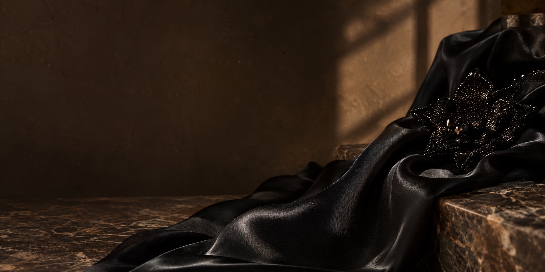 Black satin fabric with a beaded floral embellishment, styled on marble in warm light